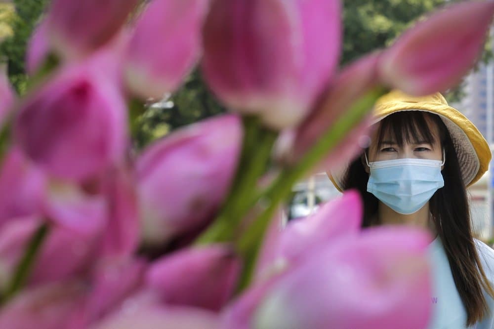 Una mujer usa una máscara 
<b>mientras camina junto a las flores de loto que se venden en una calle de <a href="https://www.univision.com/temas/china">Beijing</a></b>, el pasado 22 de julio de 2020.