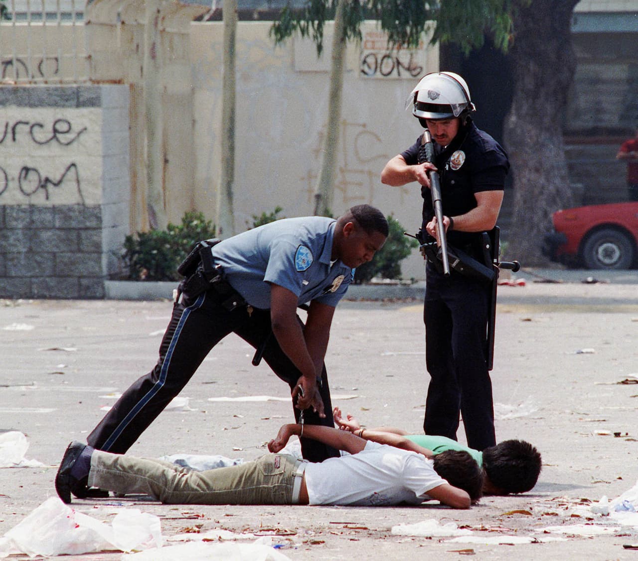 Un policía de Los Ángeles apunta con su rifle a dos sospechosos de cometer saqueos mientras los esposa un agente estatal.
