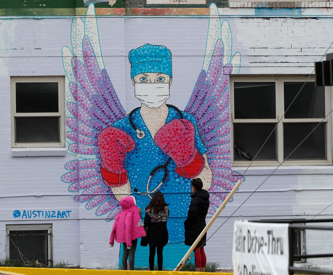 En Denver, Colorado, tres personas admiran una pintura mural de una enfermera con mascarilla y guantes de boxeo y con unas alas de ángel, representando su fuerza de luchadora por la vida y su capacidad de cuidar y sanar en momentos tan difíciles.