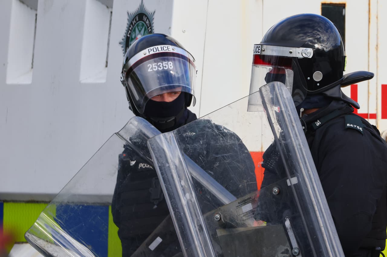 Policías con equipo antidisturbios vigilan a manifestantes cerca de Newtownabbey, en Belfast, el miércoles 10 de junio de 2026, tras un incidente con arma blanca ocurrido el lunes por la noche. (Foto AP/Peter Morrison)