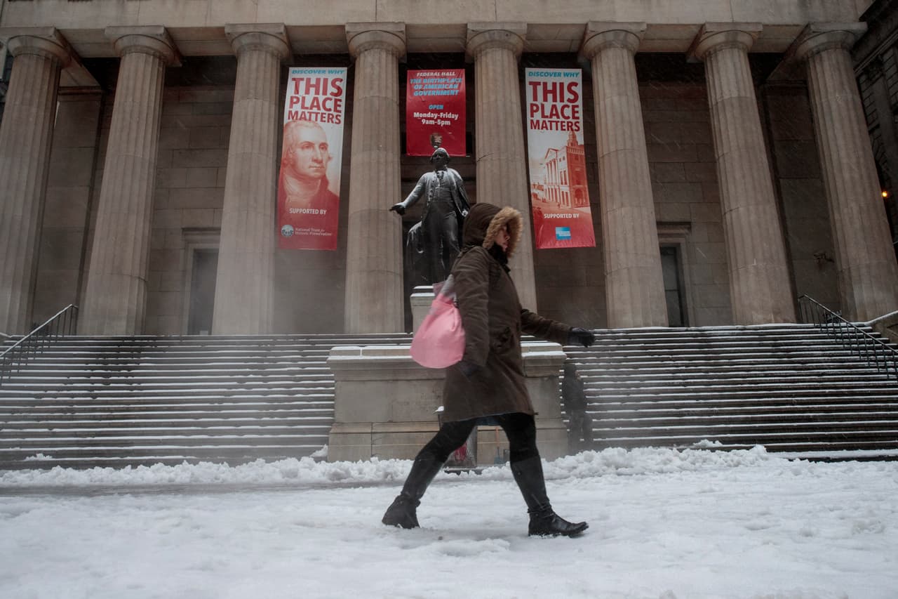 Una mujer se abre paso entre la nieve y la lluvia al caminar frente a Federal Hall.