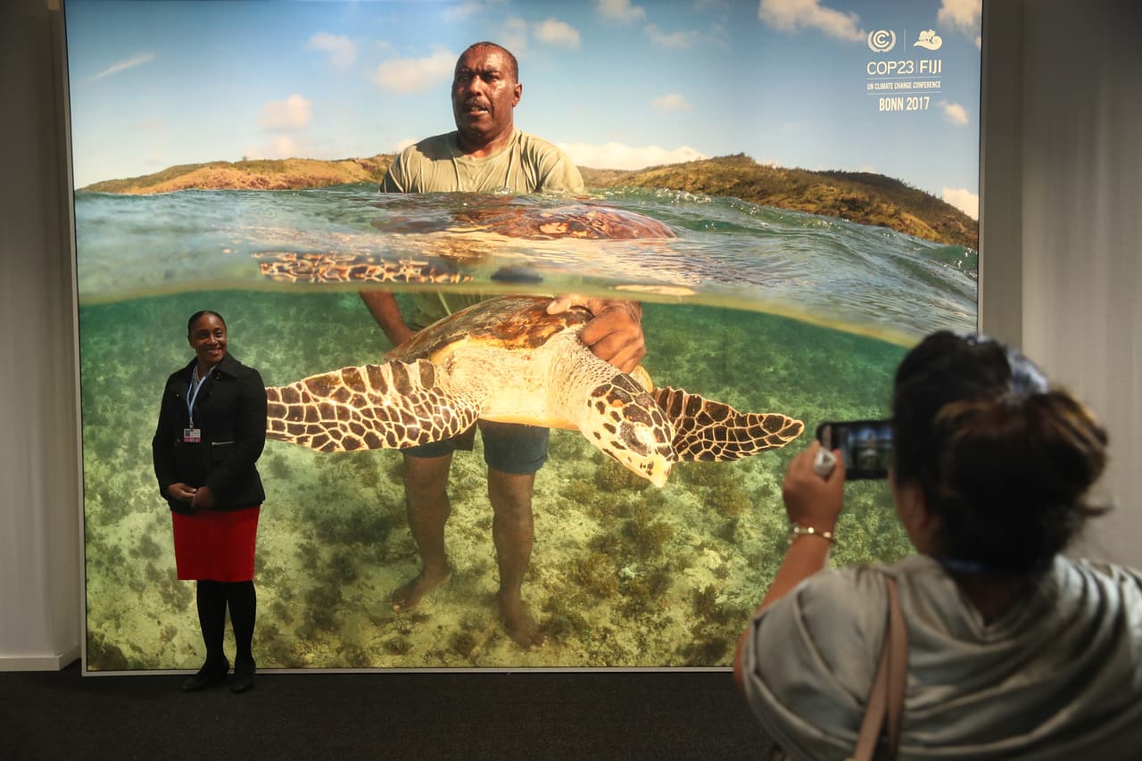 Una representante de Belice fotografía a un colega de Santa Lucía frente a una valla publicitaria iluminada que muestra a un isleño con una tortuga en Fiyi. En esta cumbre, las delegaciones de las islas tienen la aspiración de obtener más apoyo para enfrentarse al embate del cambio climático.