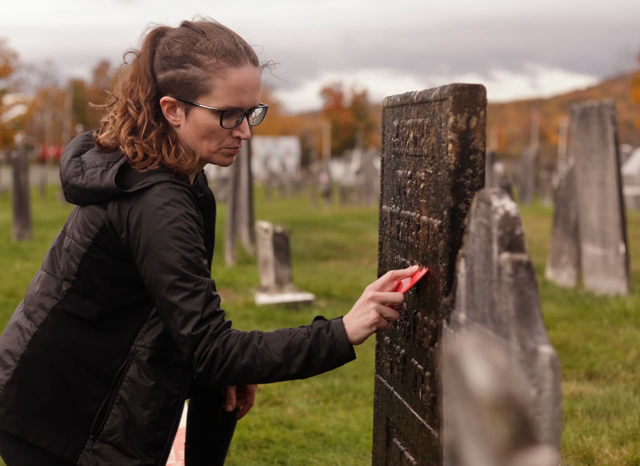 Caitlin Abrams, quien se hizo popular en TikTok por sus videos de limpieza de tumbas, retira musgo y líquenes de una lápida en un cementerio de Rupert, Vermont, el miércoles 14 de octubre de 2026.