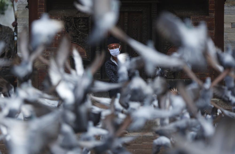 Un anciano nepalés con máscara 
<b>descansa en un templo mientras las palomas vuelan en la plaza Basantapur Durbar en Katmandú, Nepal</b>, el 22 de julio de 2020.