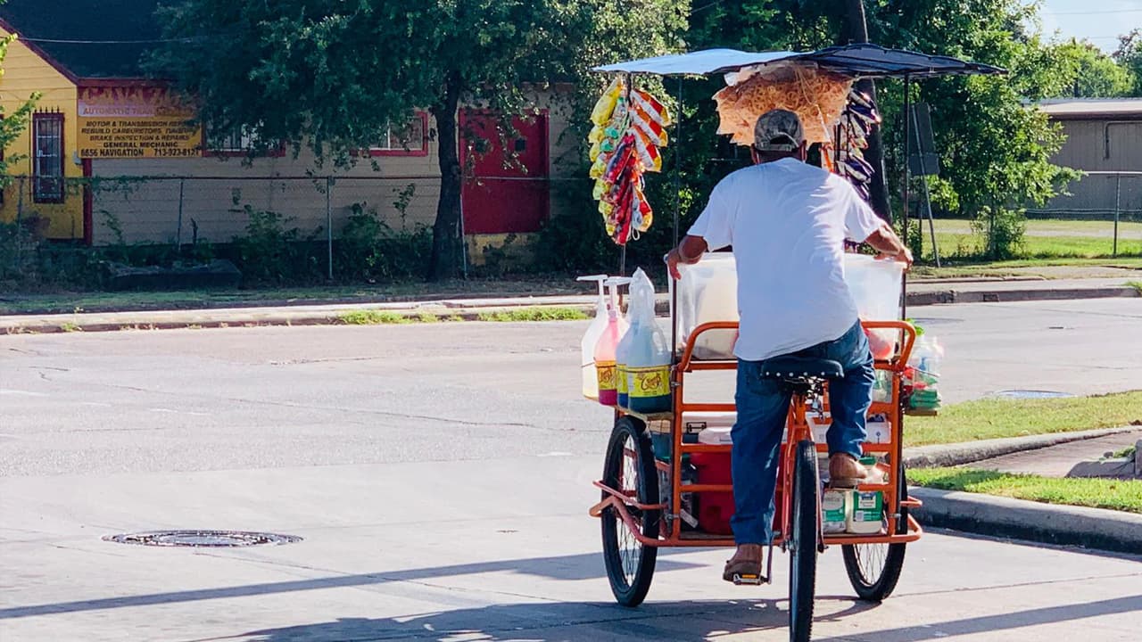 El hispano recorre las calles del barrio del East End en su bicicleta, llevando raspados y antojitos a la comunidad.