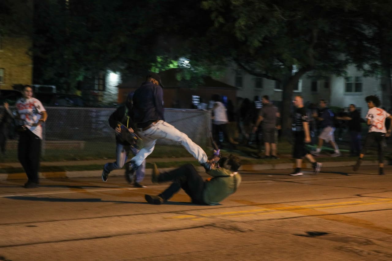 Esta fotografía es la primera de una secuencia que muestra cómo fueron heridos dos manifestantes por un civil armado con un rifle. Un video muestra que el tirador se alejaba de la muchedumbre en la calle y cayó al suelo, allí un primer manifestante se le vino encima con una patada voladora.