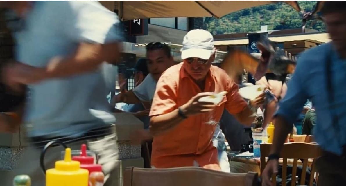 En la película se muestra el momento de pánico que viven los visitantes al parque de dinosaurios. Él aparece con gorra y toma sus margaritas mientras trata de escapar.