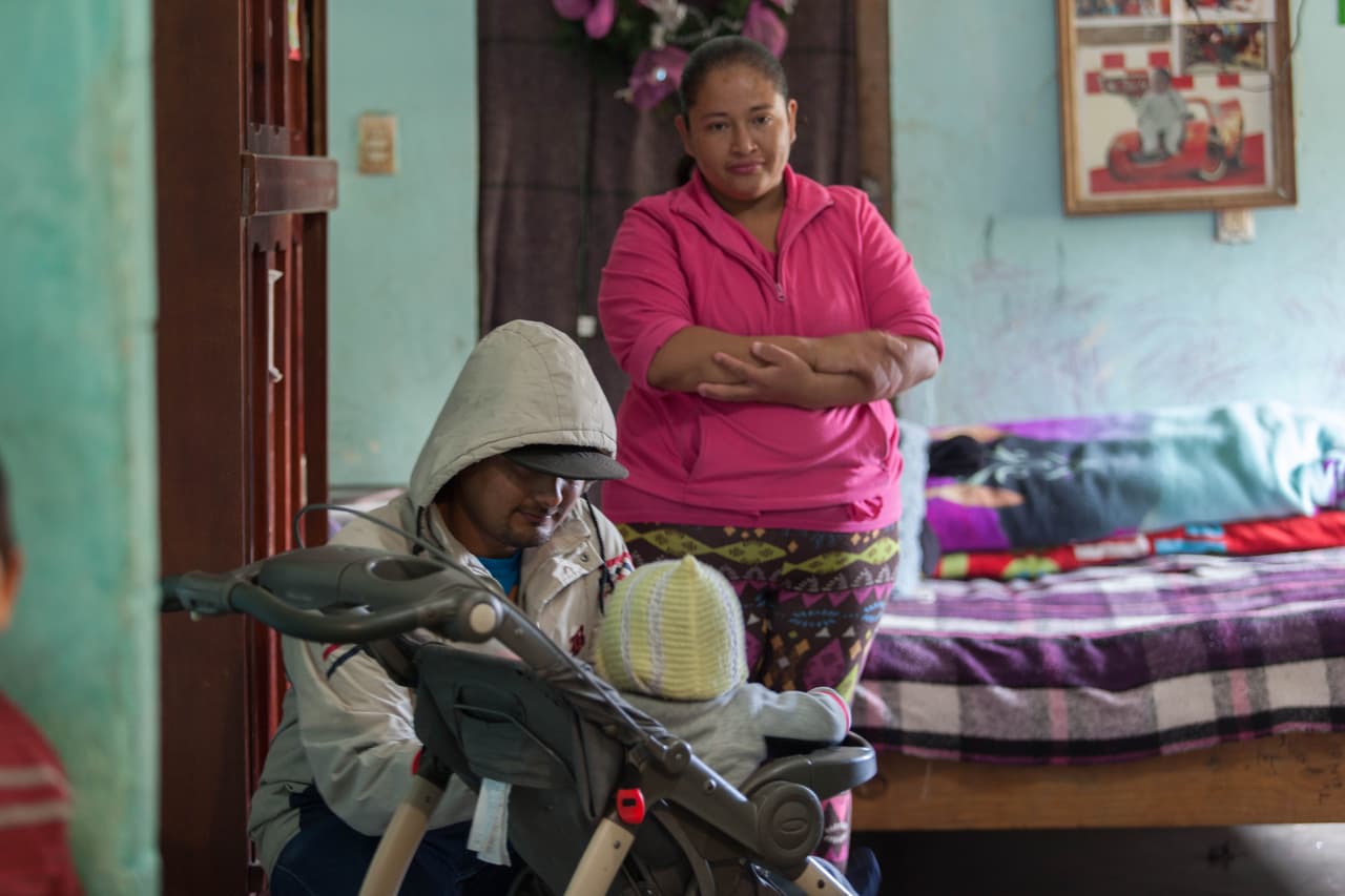 Carlos juega con su hijo menor, Jairo, dento de su casa. Atrás los observa su esposa, Elsa.