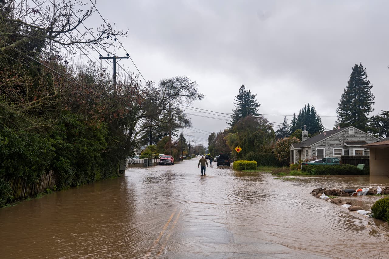 Un hombre camina por una calle inundada el viernes 10 de marzo de 2023, en Watsonville, California. Los equipos de respuesta inmediata y la Guardia Nacional rescataron a unas 56 personas durante la noche en Pájaro. Un video publicado en redes sociales mostró a un miembro de la Guardia ayudando a un conductor a salir de un coche atascado por las crecidas de agua hasta la cintura.
