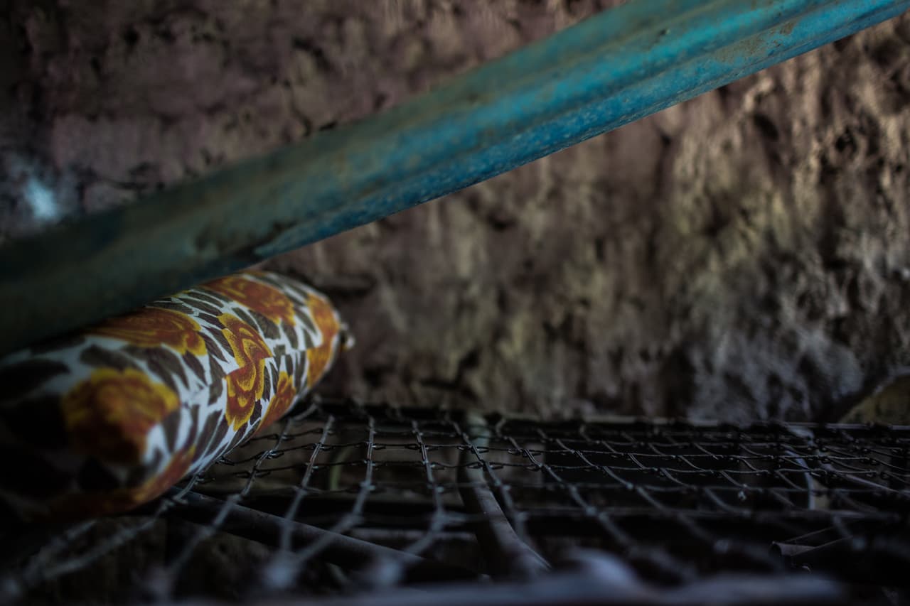 La cama donde dormía el padre de la familia, fuera de la casa que abandonaron de un día para otro. El padre dejaba que sus hijos durmieran dentro de la casa, demasiado pequeña para todo, para protegerlos: ser joven en El Salvador significa ser objeto de reclutamiento de las pandillas. Después de que el hijo de 17 años desapareciera y nunca encontraran el cuerpo, al padre de familia le amenazaron con que tenía que entregar al siguiente hijo, de 13 años, a la mara. 
<a href="https://www.univision.com/noticias/animacion-un-hijo-muerto-otro-amenazado-por-las-maras-el-drama-de-un-padre-huyendo-de-la-violencia-en-centroamerica-1-video1">Más de la historia de este padre y esta familia en esta animación. </a>