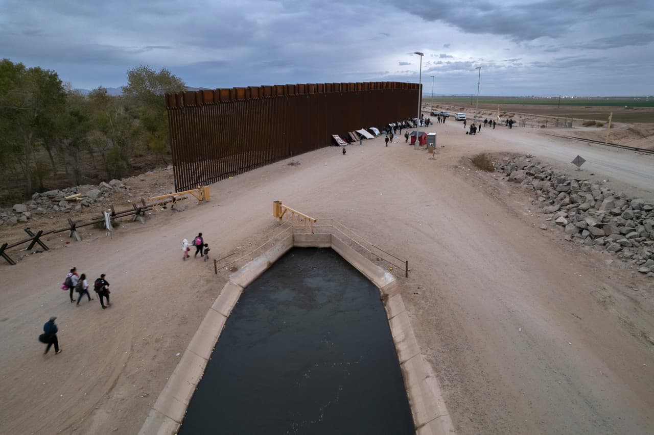 En una vista aérea, los inmigrantes caminan hacia un campamento improvisado a lo largo del muro fronterizo después de cruzar desde México a través de una brecha en la estructura en Yuma, Arizona, donde se ha visto un aumento de los cruces de migrantes en las últimas semanas, antes de la implementación del programa Quédate en México.