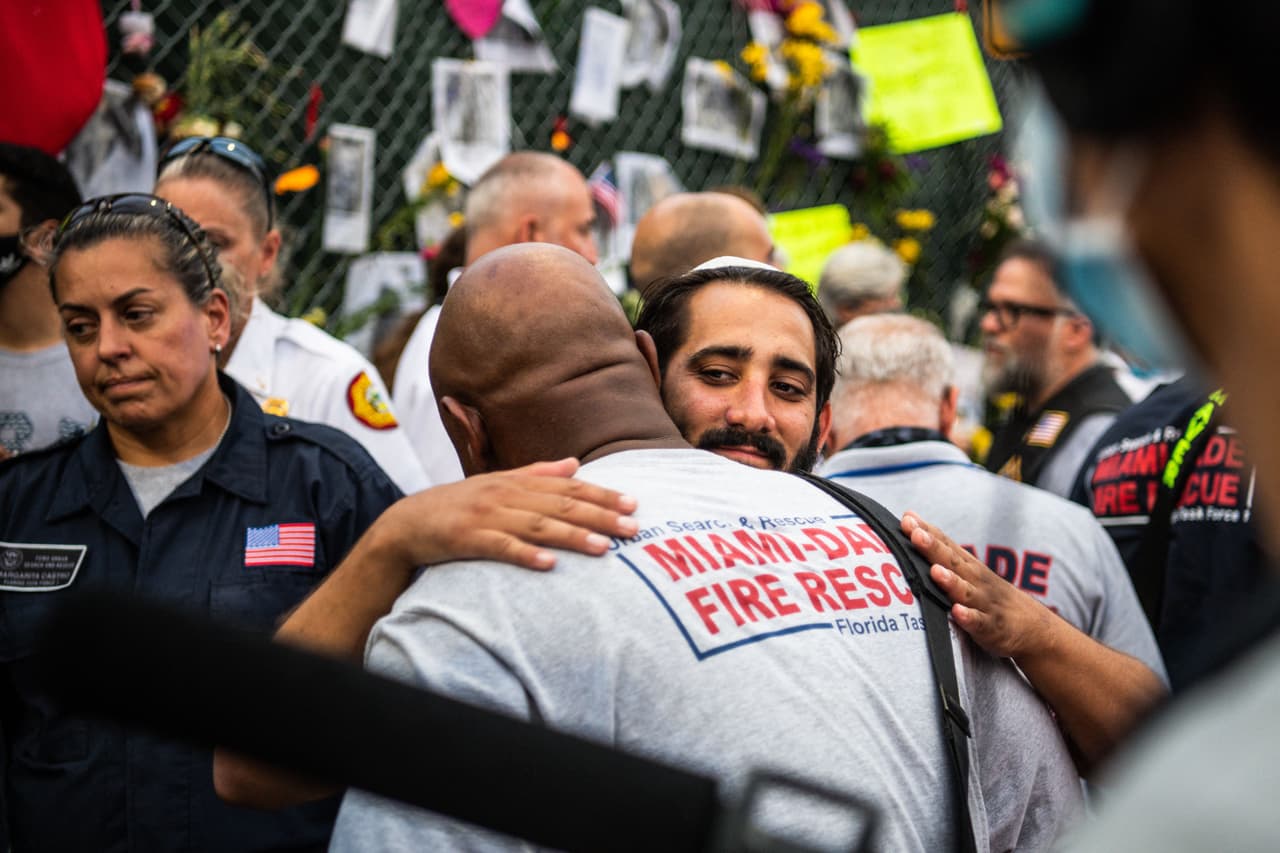 Un miembro del Miami-Dade Fire Rescue abraza a familiares y amigos de las víctimas en el improvisado memorial cerca del edificio colapsado que recuerda a las víctimas de esta tragedia.