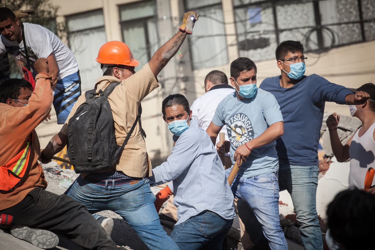 A group of civilians request silence while an expert explores under the rubble for survivors. Civilians, carrying shovels and buckets flocked to help official search and rescue teams in the earthquake aftermath. Others brought portable lights or donated water and food to rescue teams.