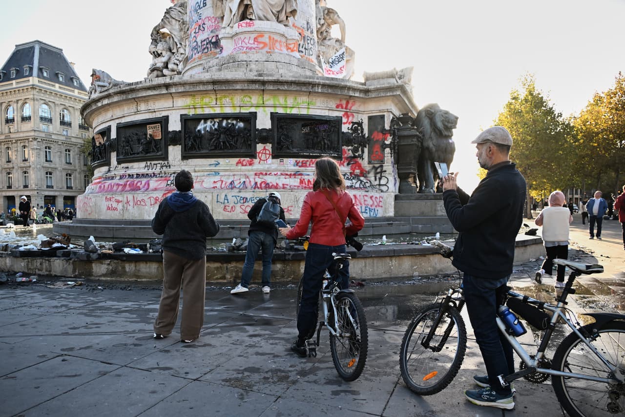 Varias personas observan los grafitis en la estatua de la Plaza de la República al día siguiente de una manifestación contra el aumento del coste de la vida, sumándose a las quejas de los estudiantes, en París, el domingo 18 de octubre de 2026