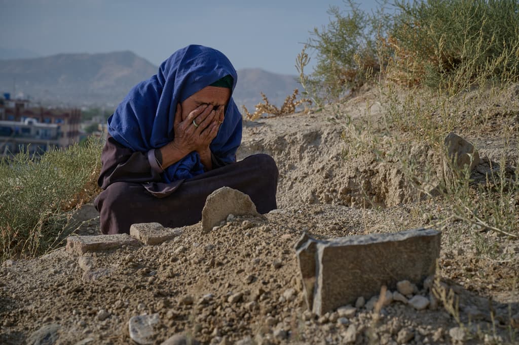 Sima se cubre el rostro ante la tumba de su nieta de seis meses —hija de su hija Diba—, fallecida durante el invierno en Kabul, Afganistán, el miércoles 12 de agosto de 2026.