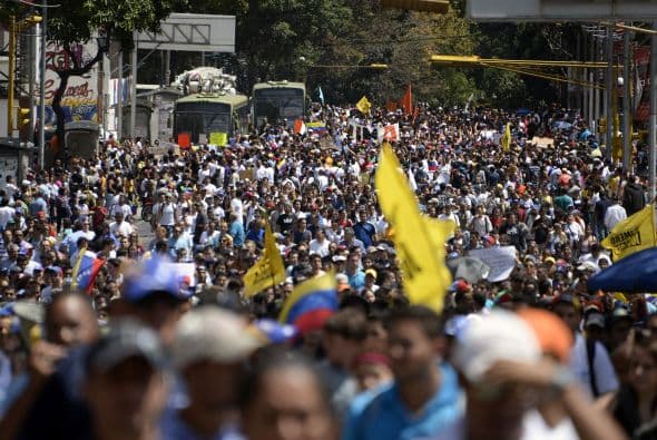 Miles de personas desarmadas toman parte en la protesta. La bandera amarilla es del grupo Primero Justicia. Los estudiantes llevaron a cabo una manifestación pacífica contra el régimen del mandatario Nicolás Maduro el 12 de febrero de 2014. Motorizados uniformados y con sus caras cubiertas, dispararon contra los manifestantes, matando a dos estudiantes y a un oficial.