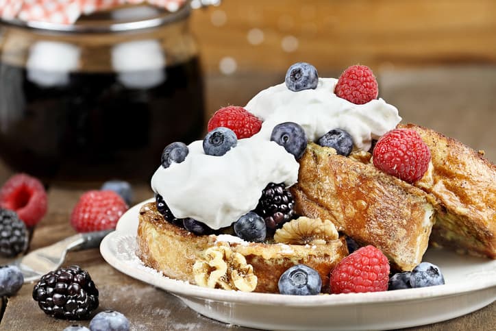 Delicious golden french toast with fresh blackberries, raspberries, blueberries, powdered sugar and whipped cream. Extreme shallow depth of field.