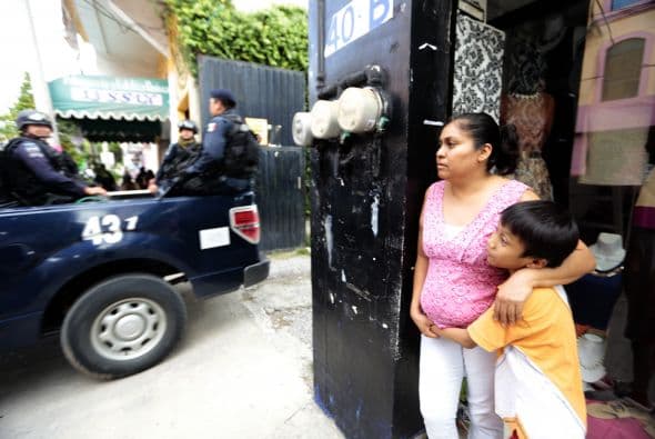 Un niño acompañado de una mujer observan a elementos de la policía federal mientras transitan.