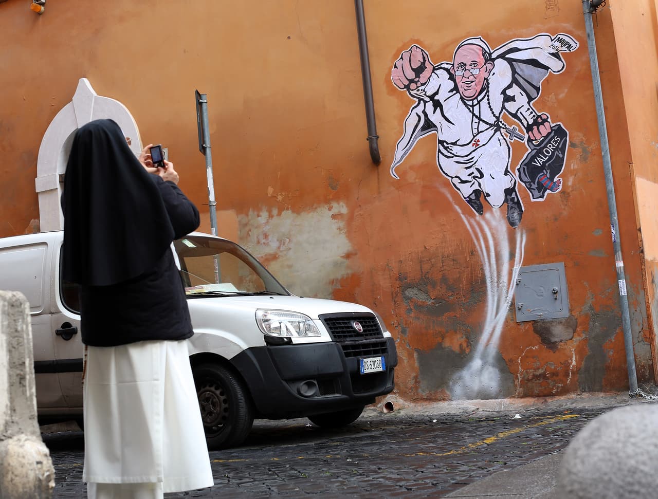 Una monja toma una foto de un grafiti que muestra al papa Francisco volando como súper héroe, en una calle de Roma, Italia.