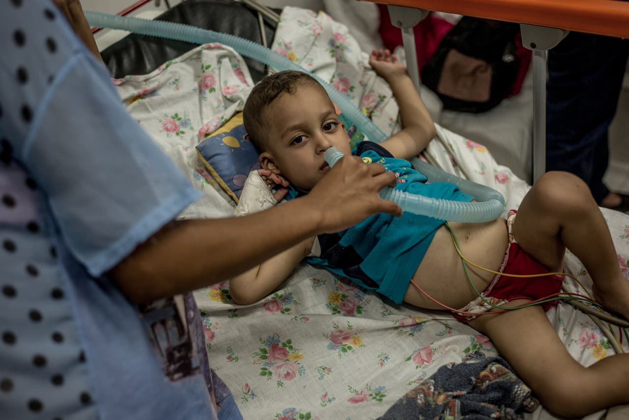 Un pequeño con problemas respiratorios recibe oxígeno directamente de la manguera, que un familiar coloca frente a su nariz en una habitación del hospital, por falta de mascarillas y otros insumos.