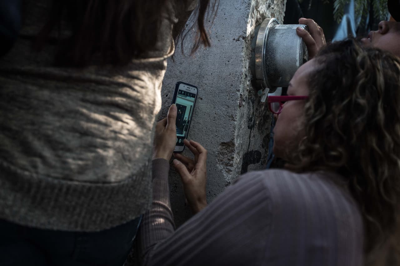 Una mujer graba la puerta de la casa de los Ibarra a través de un agujero en el muro que la rodea.