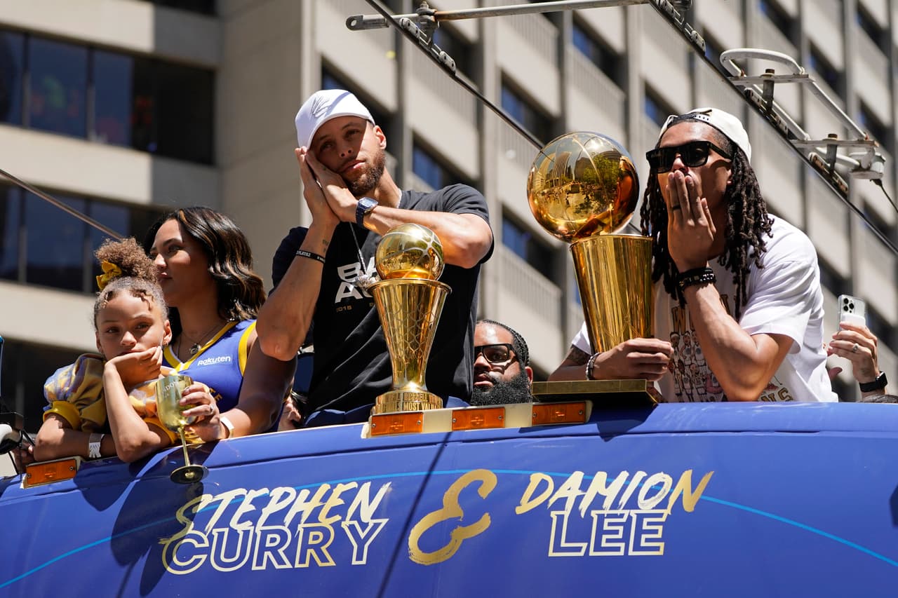 Stephen Curry y Damion Lee, a la derecha, viajan sobre un autobús durante el desfile del campeonato de la NBA Golden State Warriors en San Francisco, el lunes 20 de junio de 2022. (Foto AP/Eric Risberg)
