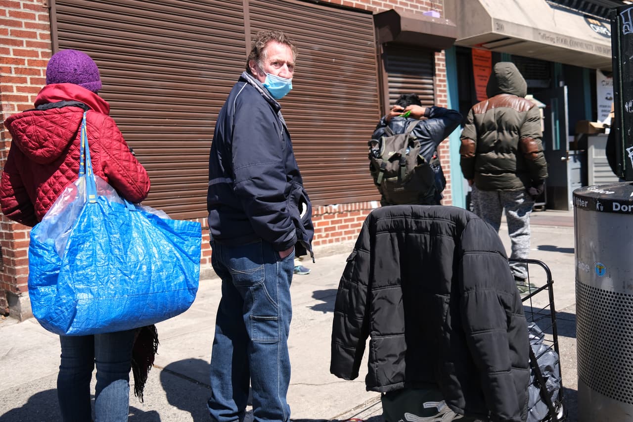<b>28 de abril -</b> Un hombre enmascarado espera en la cola para recibir comida en un banco de alimentos en Brooklyn