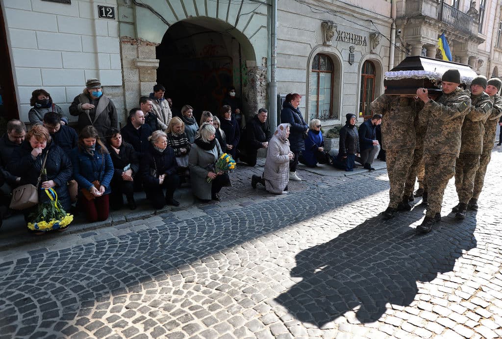 Ucranianos se arrodillan mientras ven pasar el ataúd de Rurak. A un mes del inicio de la invasión rusa a Ucrania, cientos de miles de soldados y ciudadanos de ese país han fallecido en combate o mientras intentaban huir.