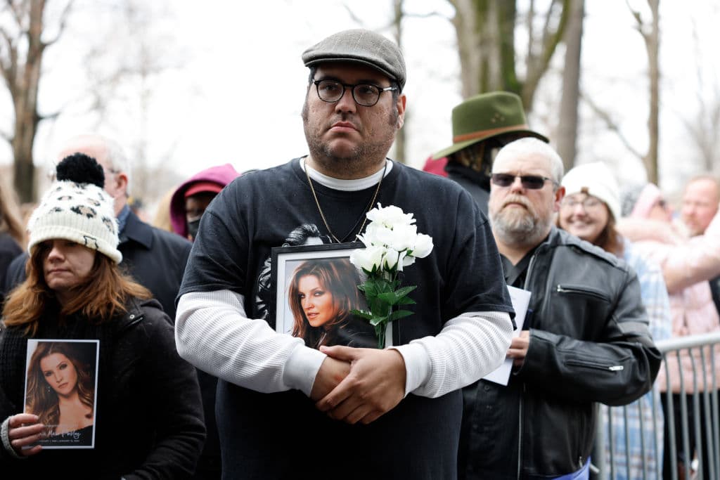 Con un ramo de flores blancas y una fotografía, otro de los asistentes escucha la ceremonia.
