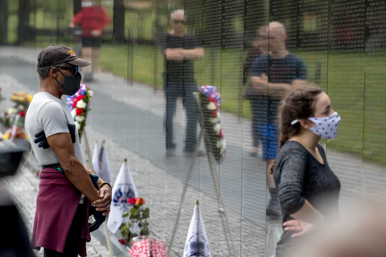Un hombre usa una máscara facial mientras él y otros visitan el Memorial de Vietnam en el Día de los Caídos en Washington.