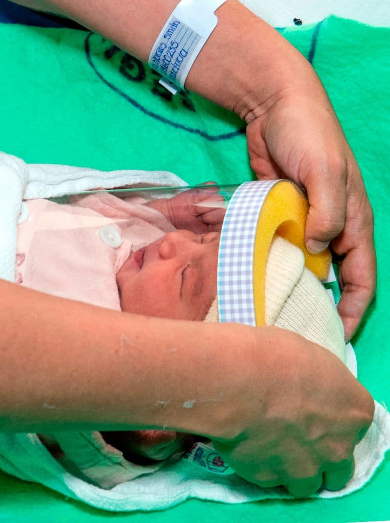 Una mujer coloca protector facial a su bebé recién nacido en la unidad de Neonatología.
