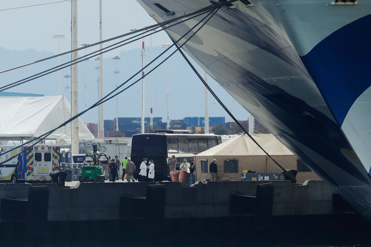 Autobuses y ambulancias esperan al pie del Grand Princess para comenzar a trasladar a los primeros pasajeros en abandonar el crucero.