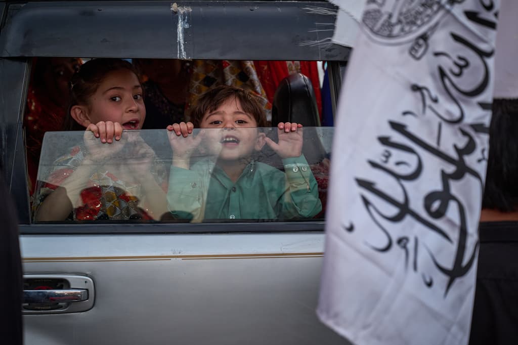 Unos niños pequeños observan desde un automóvil mientras se sostiene una bandera talibán cerca de allí.
