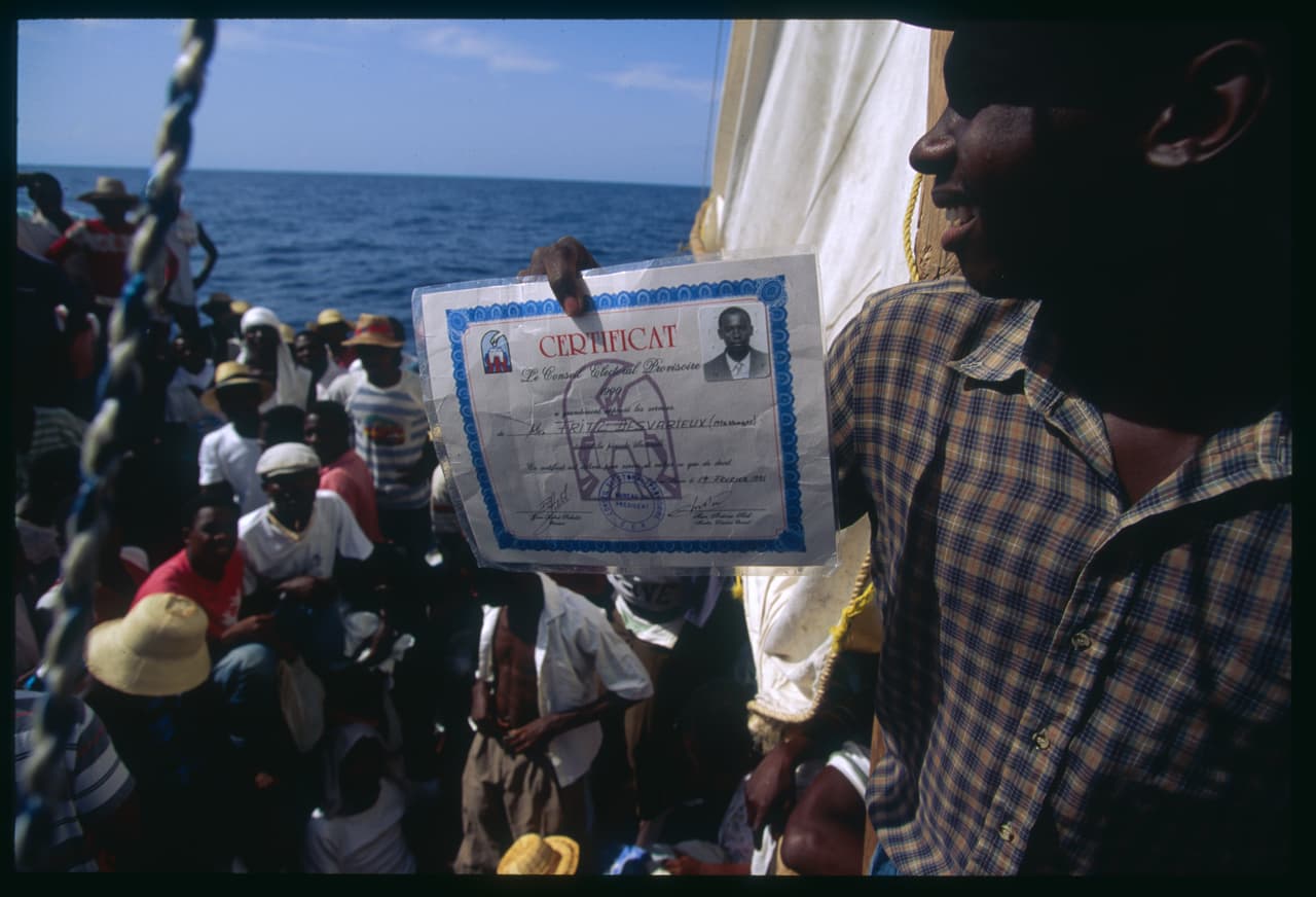 Un migrante muestra su identificación electoral de Haití durante la travesía hacia Estados Unidos por el mar caribe a principios de 1992. Entonces varias embarcaciones repletas de migrantes haitianos fueron interceptados por la Guardia Costera estadounidense y enviados de regreso a su país.