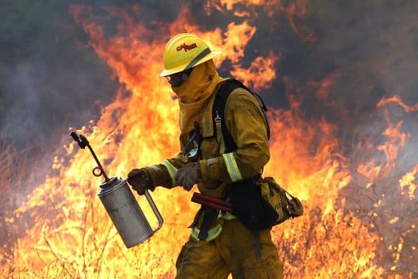 Un bombero se aleja de una llama alta mientras intentaba quemar la hierba para evitar que el fuego se propague.