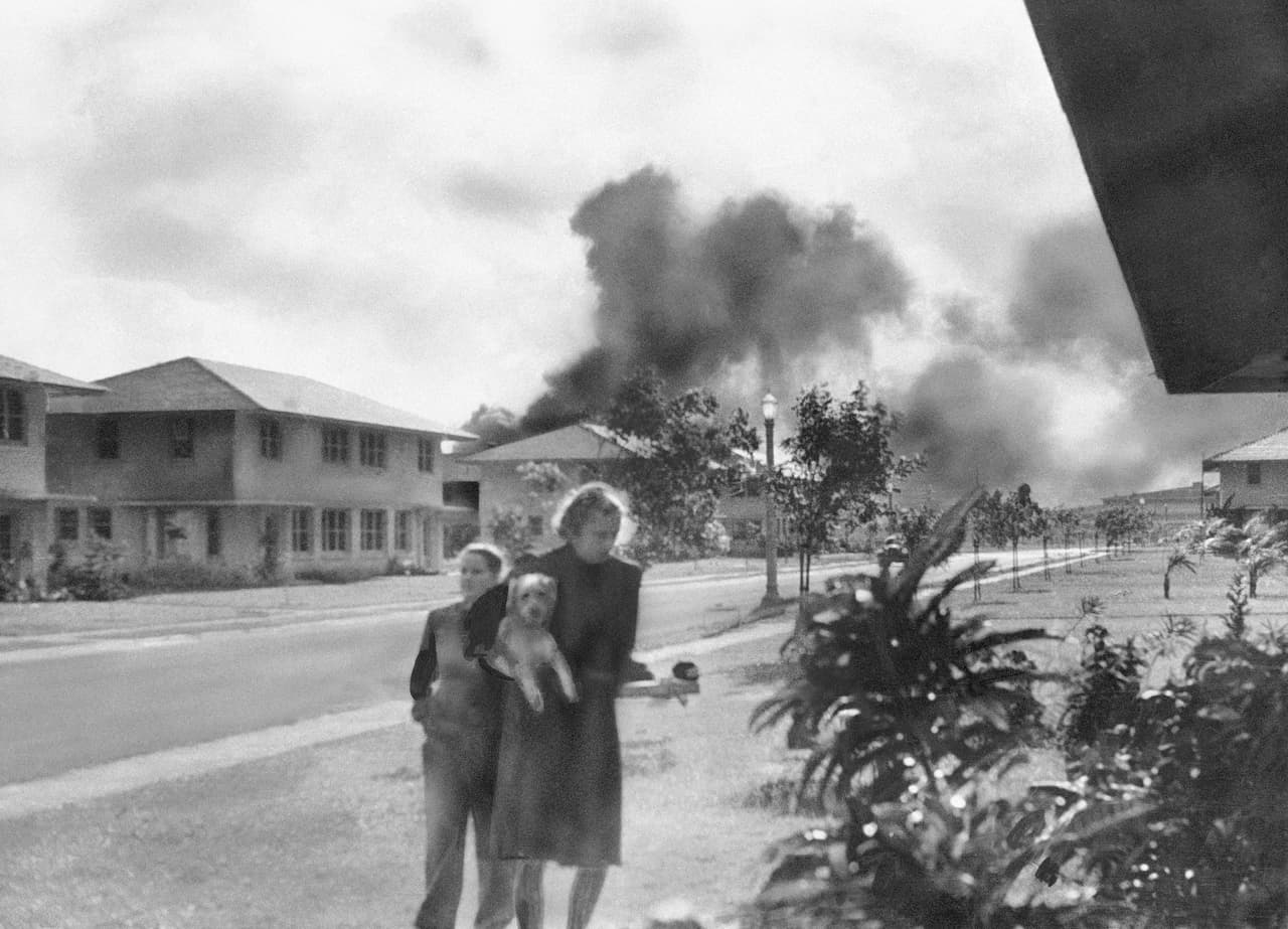 Esta fotografía muestra a la esposa de un oficial no identificado que vio el humo del ataque a la distancia, a las 8:15 AM del 7 de diciembre de 1941. Su vecina, Mary Naiden, entonces azafata del ejército (y quien tomó la foto), le dijo: “Hay círculos rojos en esos aviones en lo alto. ¡Son japoneses!
<br>