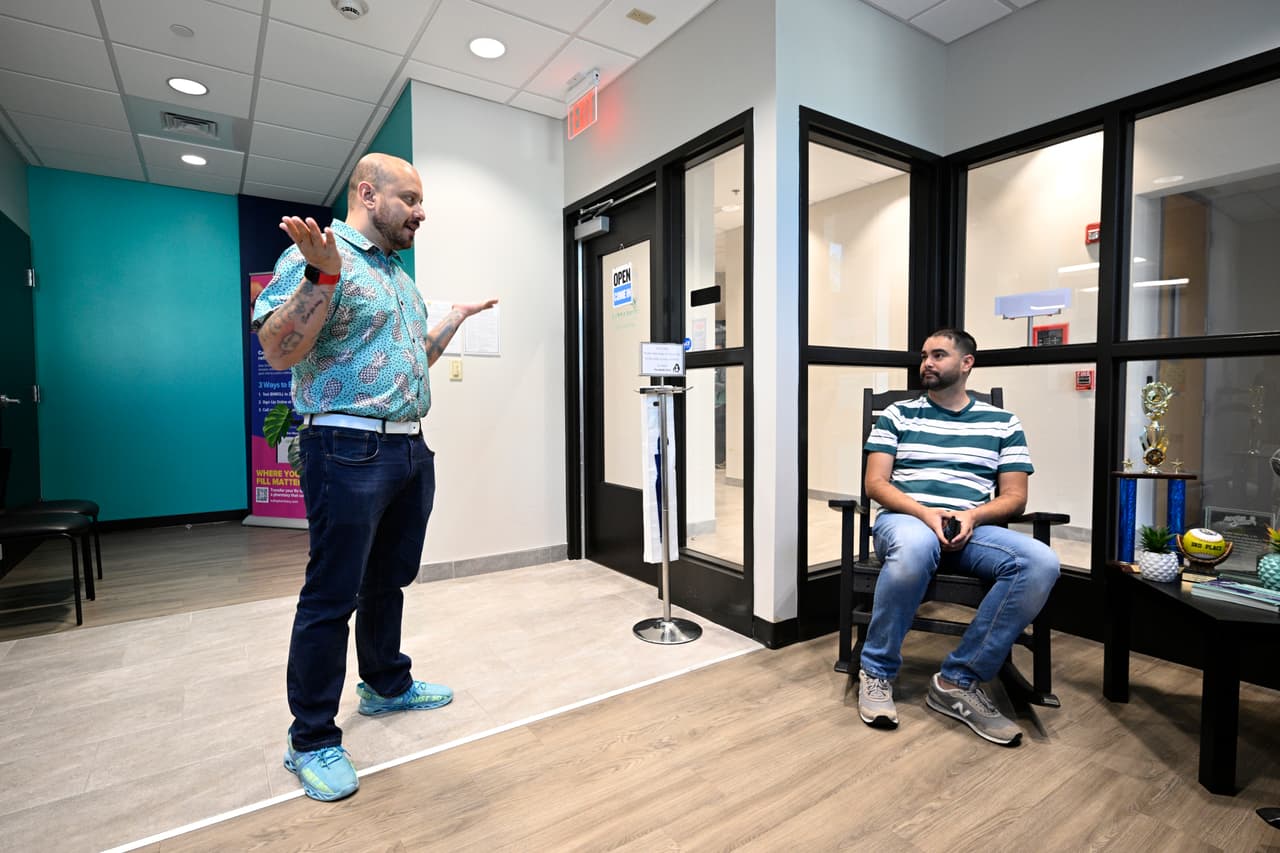 Andres Acosta Ardila (izq.), director de relaciones comunitarias de Pineapple Healthcare, saluda a Fernando Hermida mientras espera su cita en la clínica médica de Orlando, Florida, el 28 de mayo de 2024.