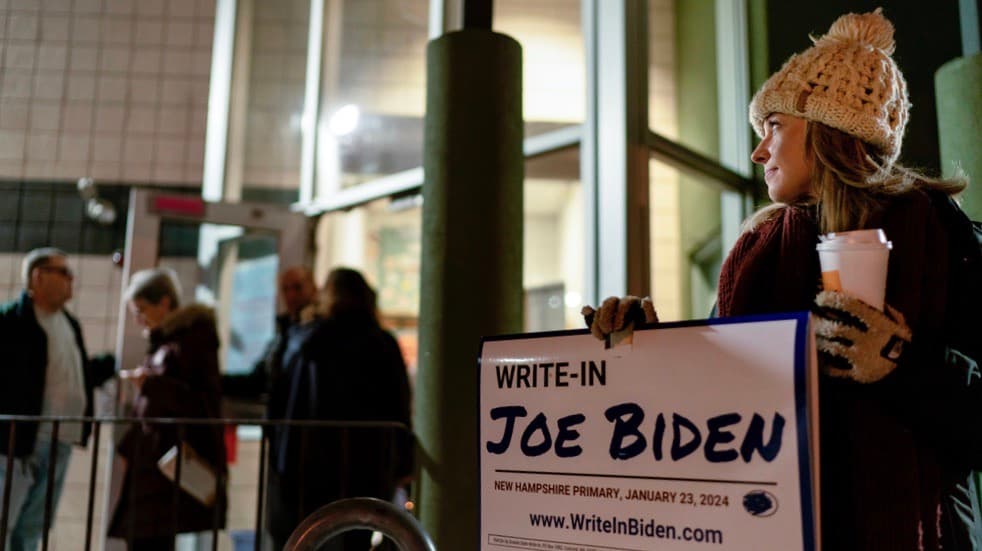 La voluntaria Ashley Marcoux afuera de un centro de votación con un cartel de campaña que apoya al presidente Joe Biden como candidato por escrito para las primarias presidenciales de New Hampshire en Manchester, Nuevo Hampshire, el martes 23 de enero de 2024.