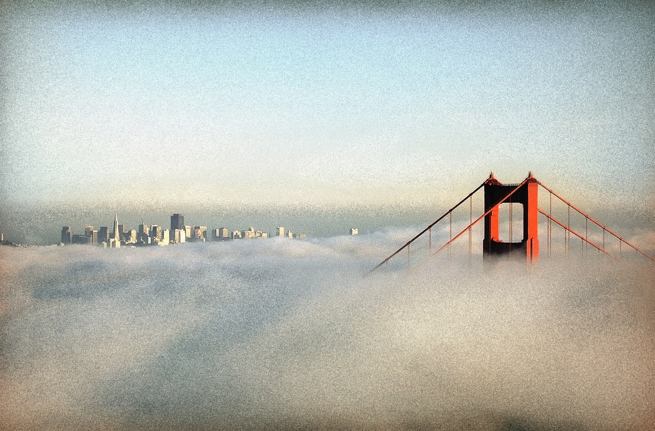 <b>Su color. </b>Su distintivo naranja brillante son la elección del arquitecto consultor Irving Morrow. Se basó en la combinación de colores fríos del entorno natural del puente y en proporcionar mayor visibilidad para los buques que pasan. Si hubiera sido por la Marina de EEUU
<b>el Golden Gate podría haber sido pintado con rayas negras y amarillas</b> para asegurar aún mayor visibilidad.Una fotografía tomada en 1995, un día nublado sobre la bahía que apenas deja ver la punta de las torres del puente. Al fondo la ciudad de San Francisco.
<br>