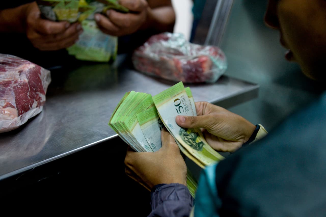 Una mujer cuenta un fajo de billetes para hacer una pequeña compra en una carnicería de Caracas.