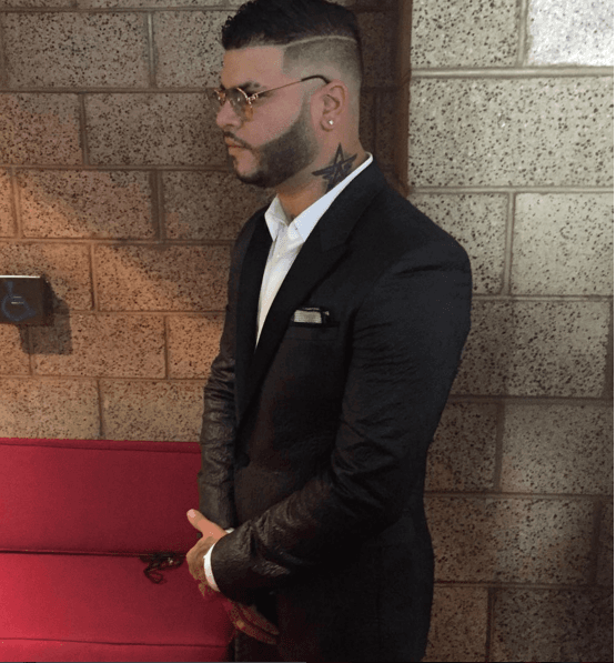En este look lleva traje muy formal, sin corbata, pero con unos lentes que le van increíbles con la barba.