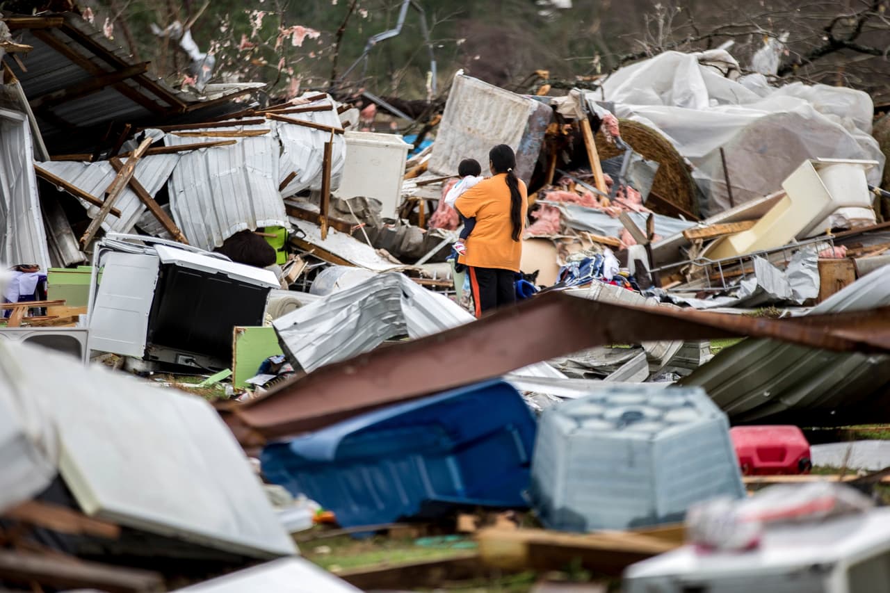 Una mujer sostiene a un niño mientras que camina a través de una granja que fue dañada por un tornado.