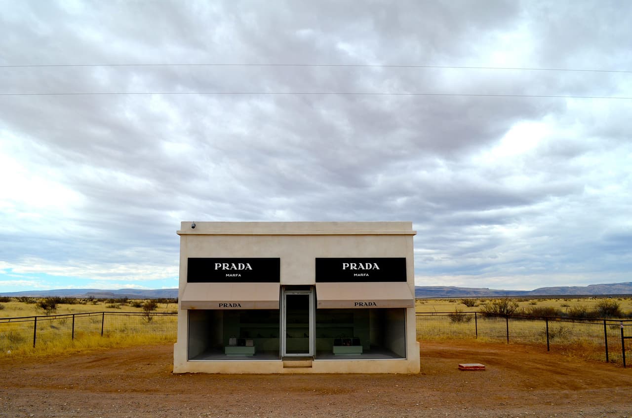 Esta pequeña tienda se ha convertido ya en un icono popular.
<a href="http://www.vogue.com/872499/prada-marfa-visit-texas-elmgreen-dragset-art-vandalism/">Diseñada por Michael Elmgreen e Ingar Dragset</a>, la instalación artística sirve para ironizar sobre el capitalismo y el culto a las marcas. Se puede encontrar en un punto de la carretera US-90 cerca de Marfa, casi literalmente, en el medio de la nada. En lugar de estar rodeada de otras boutiques de lujo, lo más cercano que tiene es una oficina de correos.
<br>