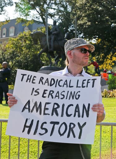 Un manifestante en contra de la remoción de la estatua sostiene un letrero en el que se lee "La izquierda radical está borrando la historia americana".