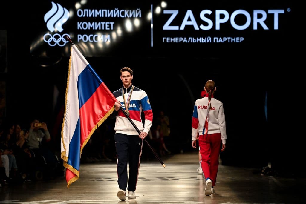 Models, one holding a Russian flag, present the Russian Olympic Team uniform for the Tokyo 2020 Olympic Games, designed and manufactured by ZASPORT clothing company, in Moscow on April 14, 2021. (Photo by Kirill KUDRYAVTSEV / AFP) (Photo by KIRILL KUDRYAVTSEV/AFP via Getty Images)