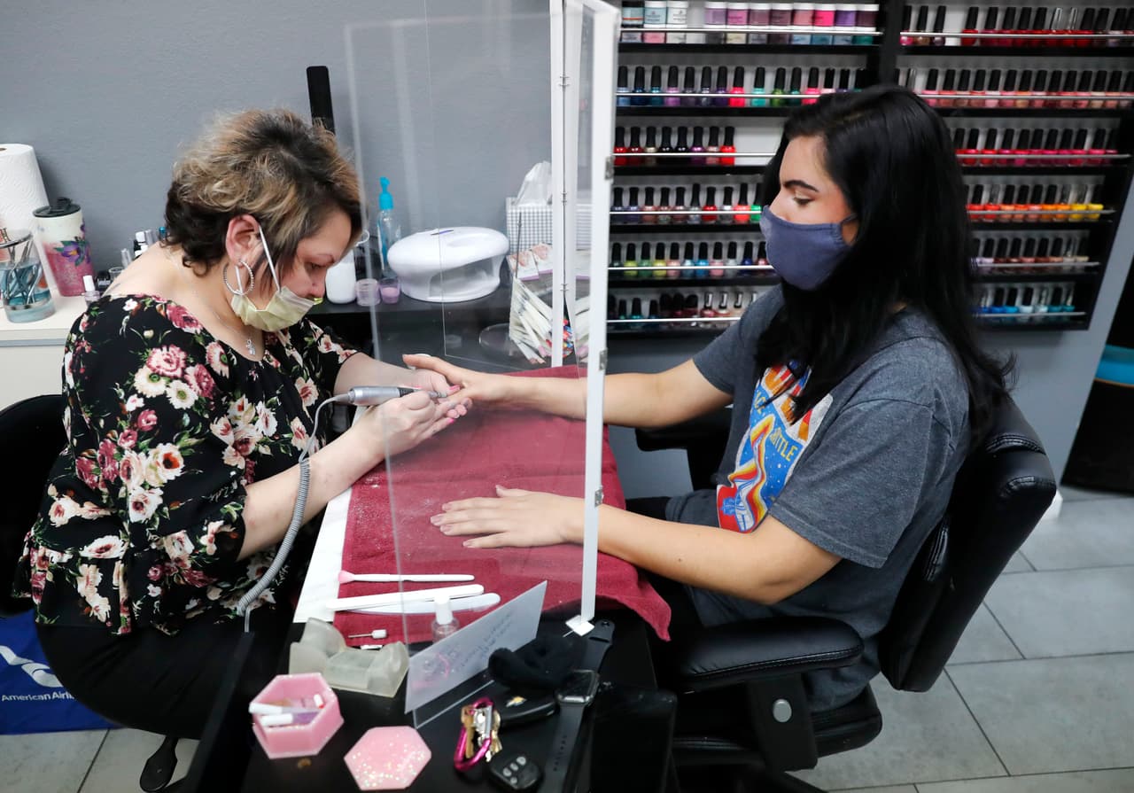 Una manicurista atiende a una clienta en un salón de belleza de Dallas, Texas, reabierto el 24 de abril. El establecimiento instaló barreras entre las manicuristas y las clientas para mantener las normas de distanciamiento.