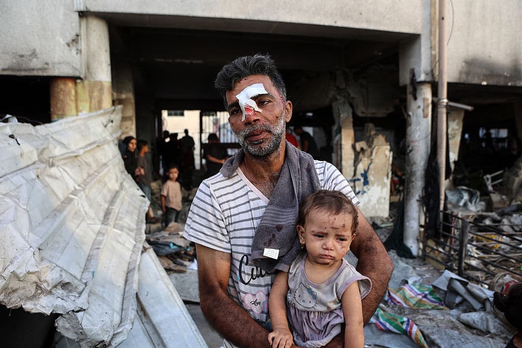 Un hombre herido carga a un niño pequeño mientras otros buscan sus pertenencias entre los escombros, en la escuela al-Farabi, convertida en refugio para palestinos desplazados tras ser alcanzada por un ataque israelí, en la ciudad de Gaza.