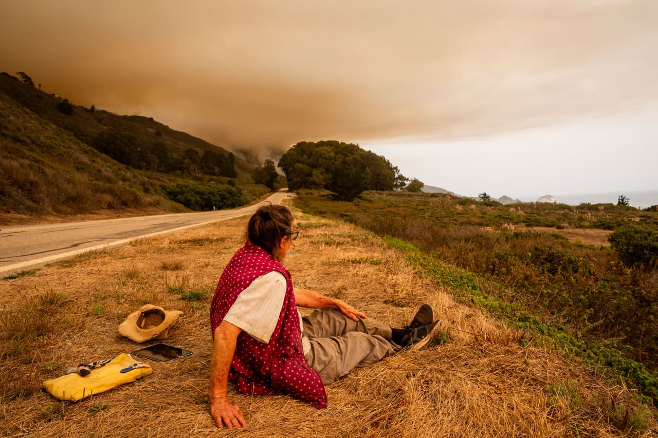 Una mujer, sentada en la tierra al lado de la carretera mientras el incendio Plaskett arde en las inmediaciones, el 28 de agosto de 2026, en Big Sur, California. (AP Foto/Ethan Swope)