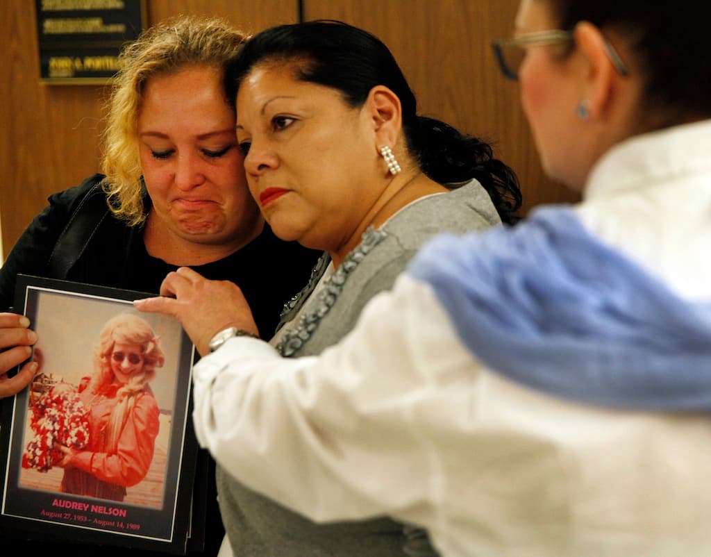 Pearl Nelson, de 38 años, con una foto de su madre, Audrey Nelson, mientras Mary Louise Frías la abraza. La madrina de Frías, Guadalupe Apodaca Zambrano, fue víctima de Little. La familia de las mujeres asesinadas se encontraban en la audiencia de sentencia de Little en el Tribunal Superior de Los Ángeles el 24 de septiembre de 2015.