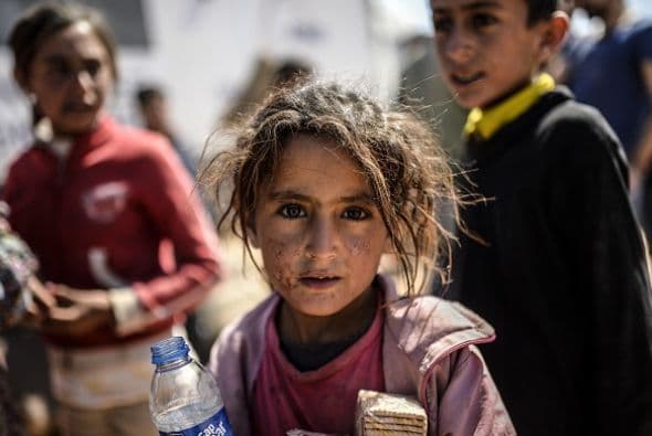 Una niña sostiene una botella de agua y un paquete de galletas. Su cara está visiblemente sucia tras el largo éxodo para llegar a la frontera de Turquía.
